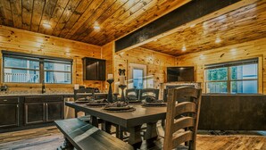 A wooden cabin interior with a dining table set for four, a bench, and a fireplace. - Stylish New 5BR 4BA Cabin Steps From Dollywood (Pigeon Forge)