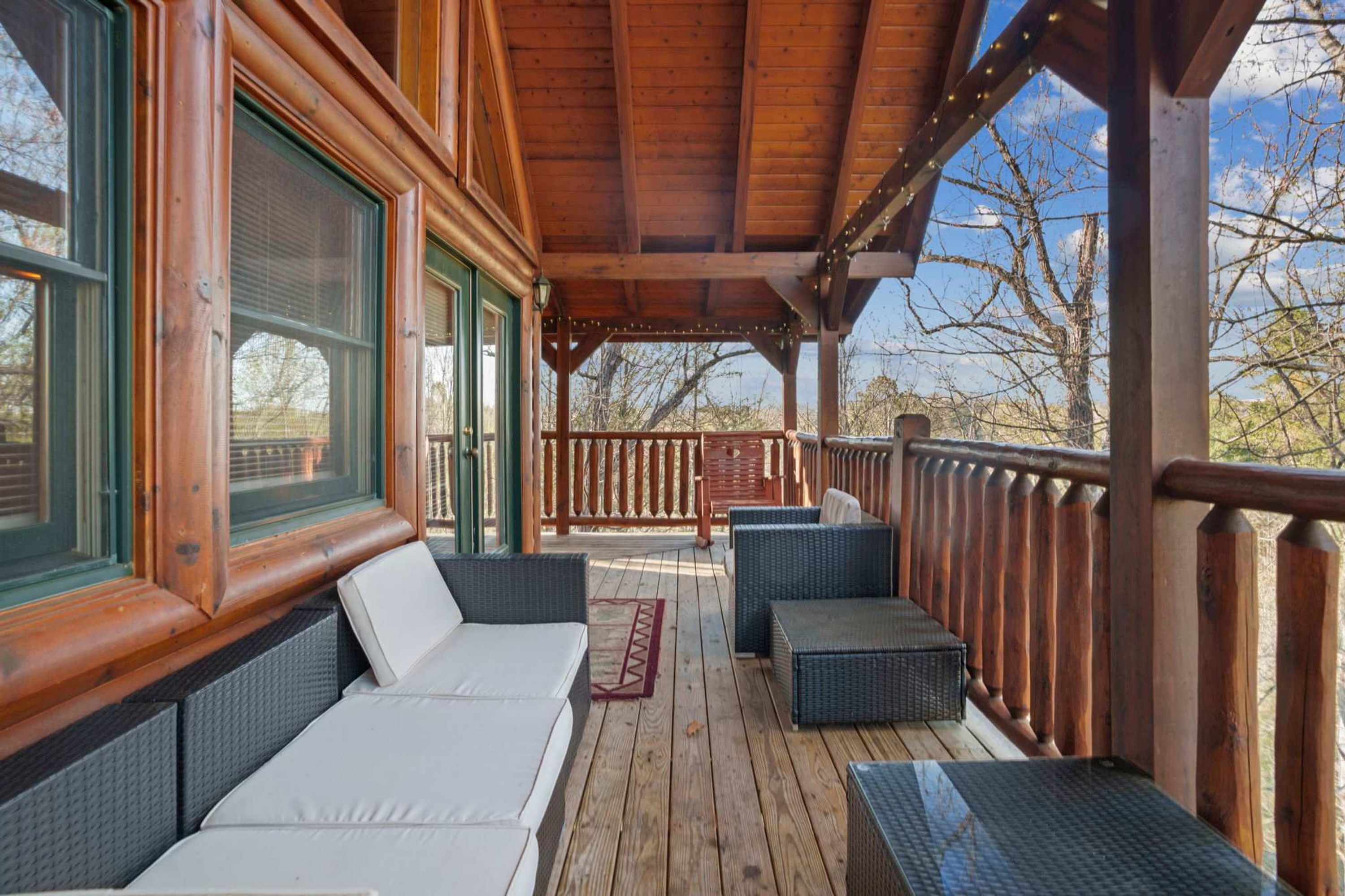 A covered porch with a wooden deck, wicker furniture, and a view of trees.