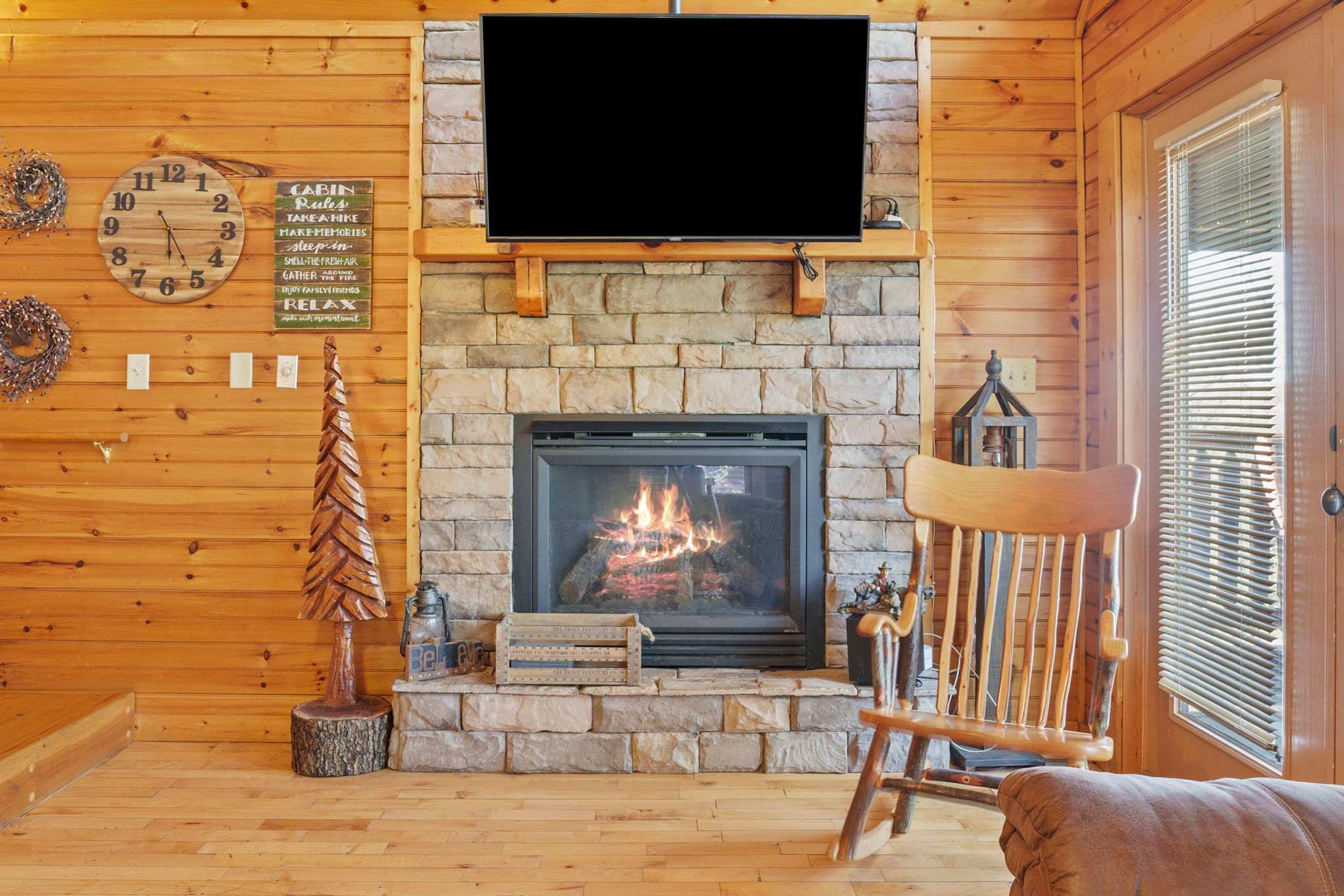 A cozy cabin interior with a stone fireplace, a mounted television, and a wooden chair.
