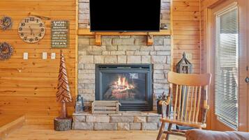 A cozy cabin interior with a stone fireplace, a mounted television, and a wooden chair.