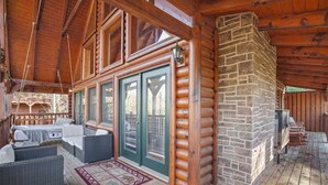 A log cabin with a covered porch, outdoor seating, and a stone fireplace. - Cozy Mountain Retreat With Private Hot Tub (Gatlinburg)