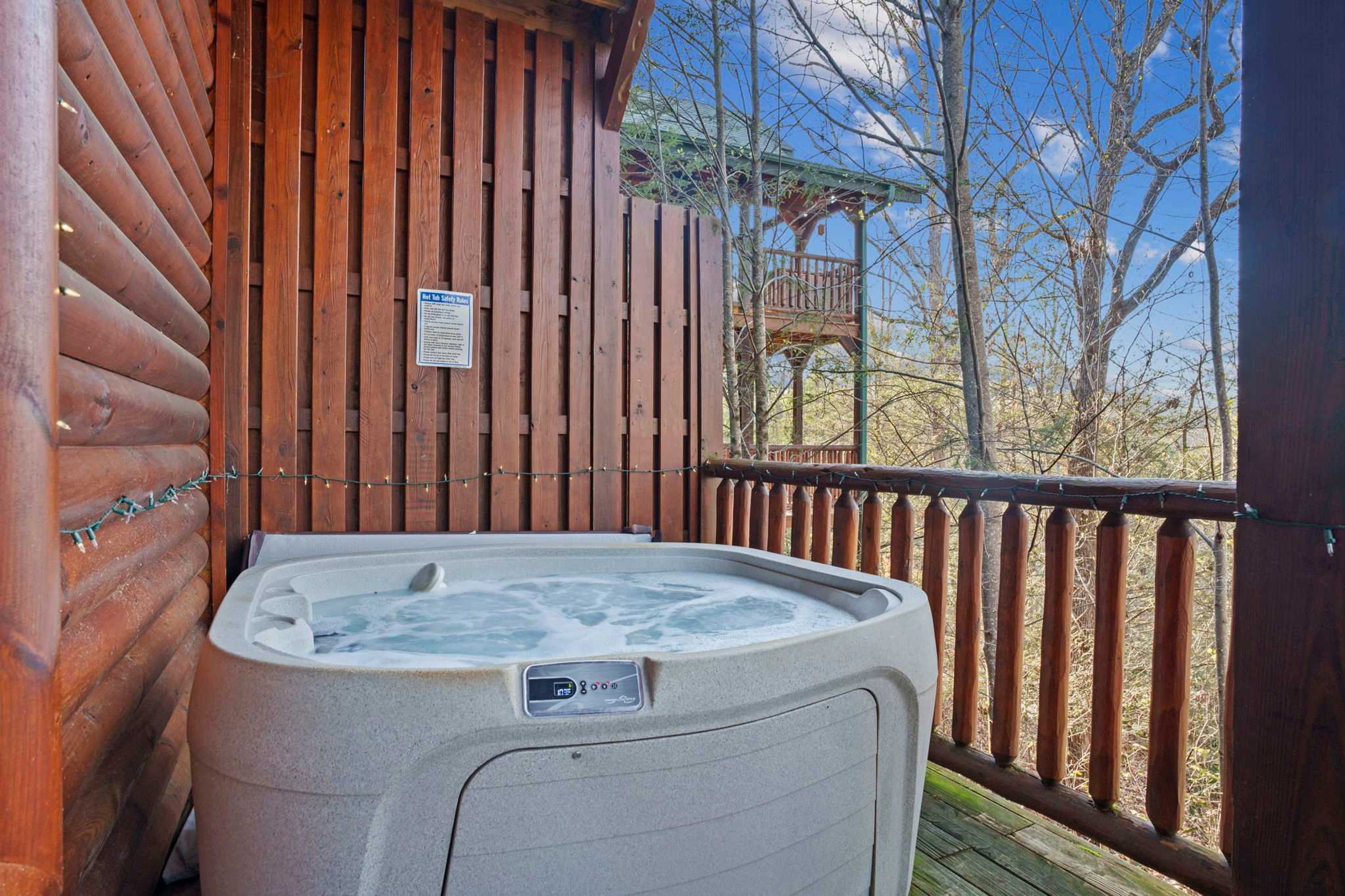 Un jacuzzi en una terraza de madera, con una valla y una estructura de madera al fondo.