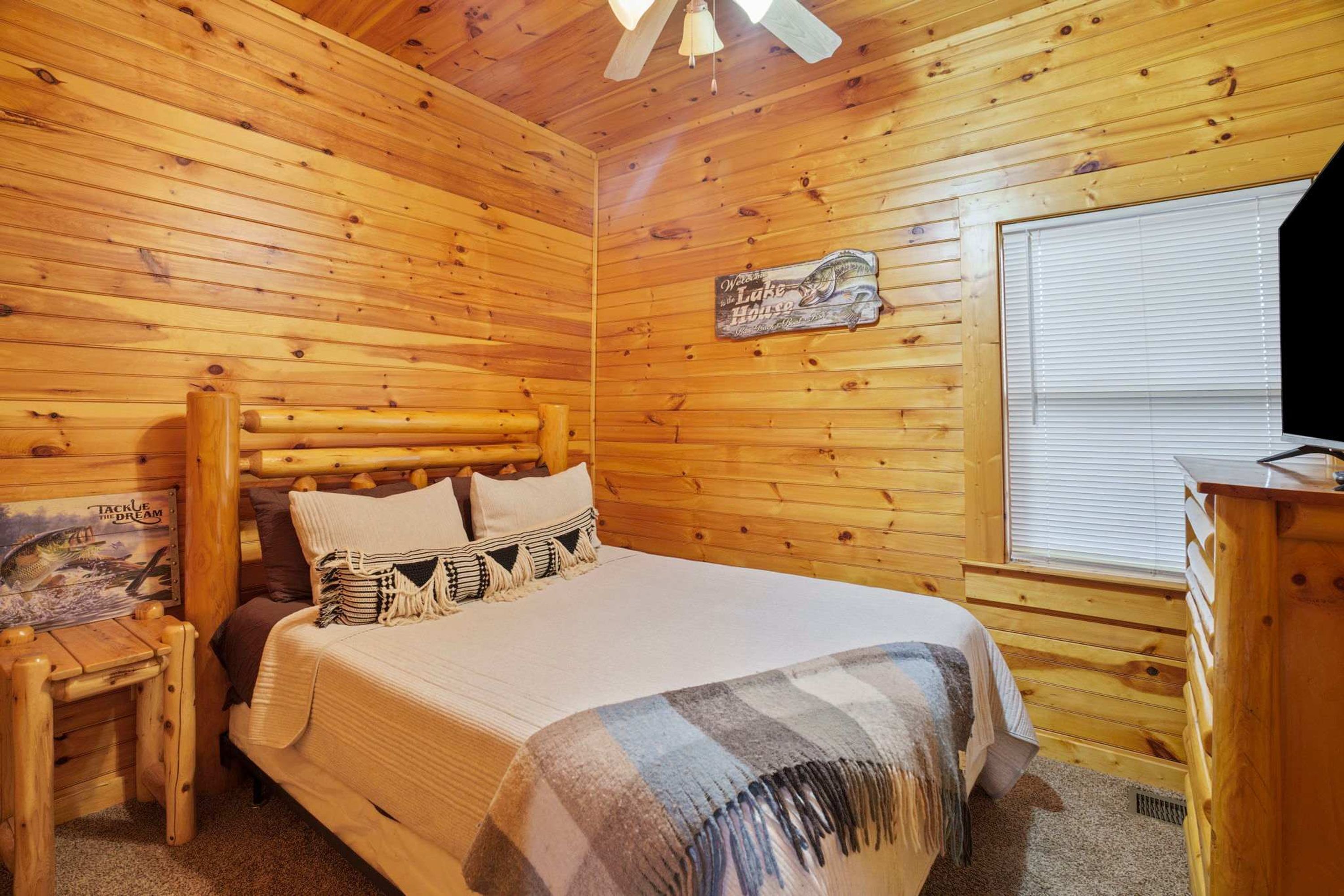 Una habitación de cabaña de madera con cama, mesita de noche, cómoda y ventana con persianas.