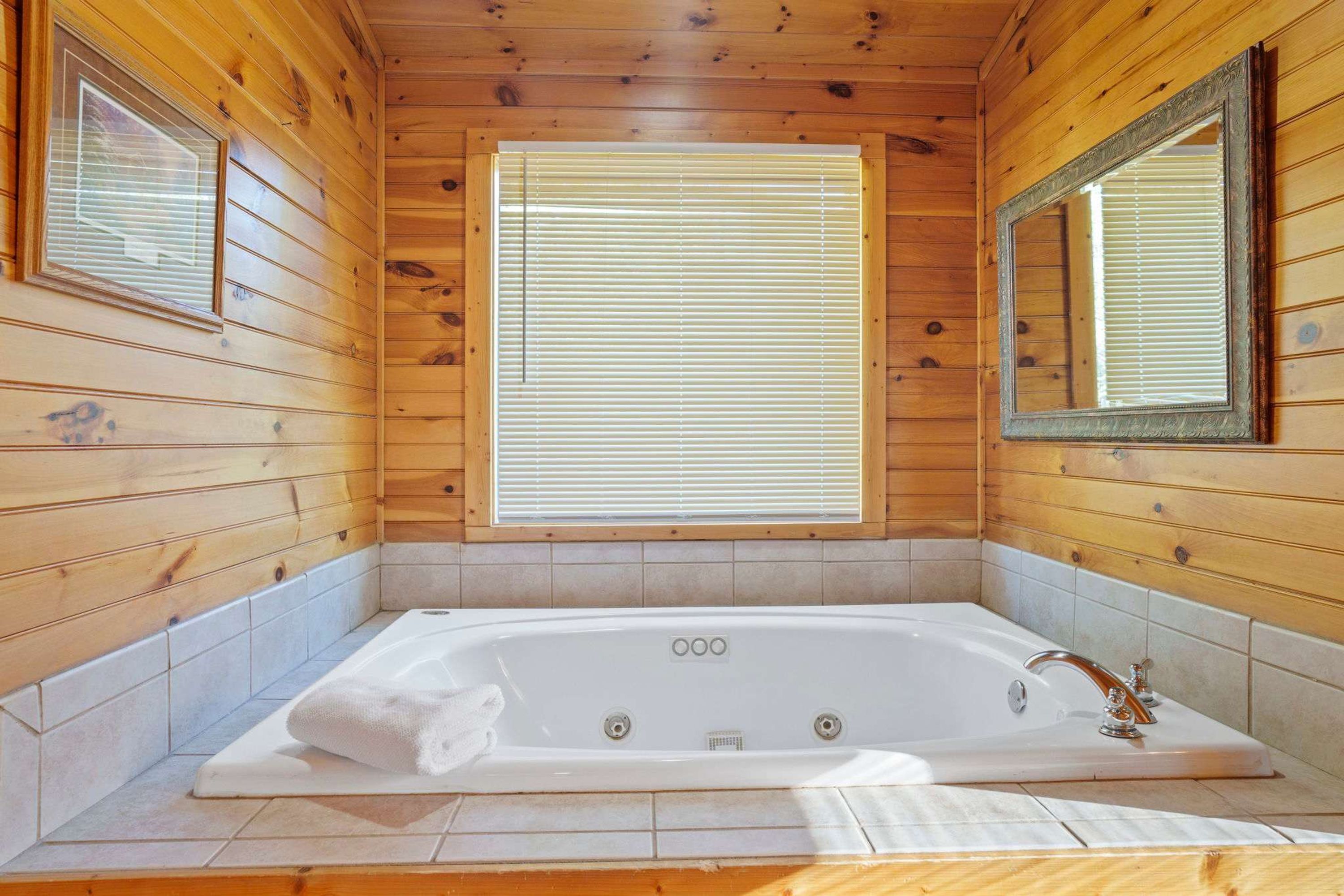 Une salle de bain rustique, avec une grande baignoire, des murs en bois et une fenêtre équipée de stores.
