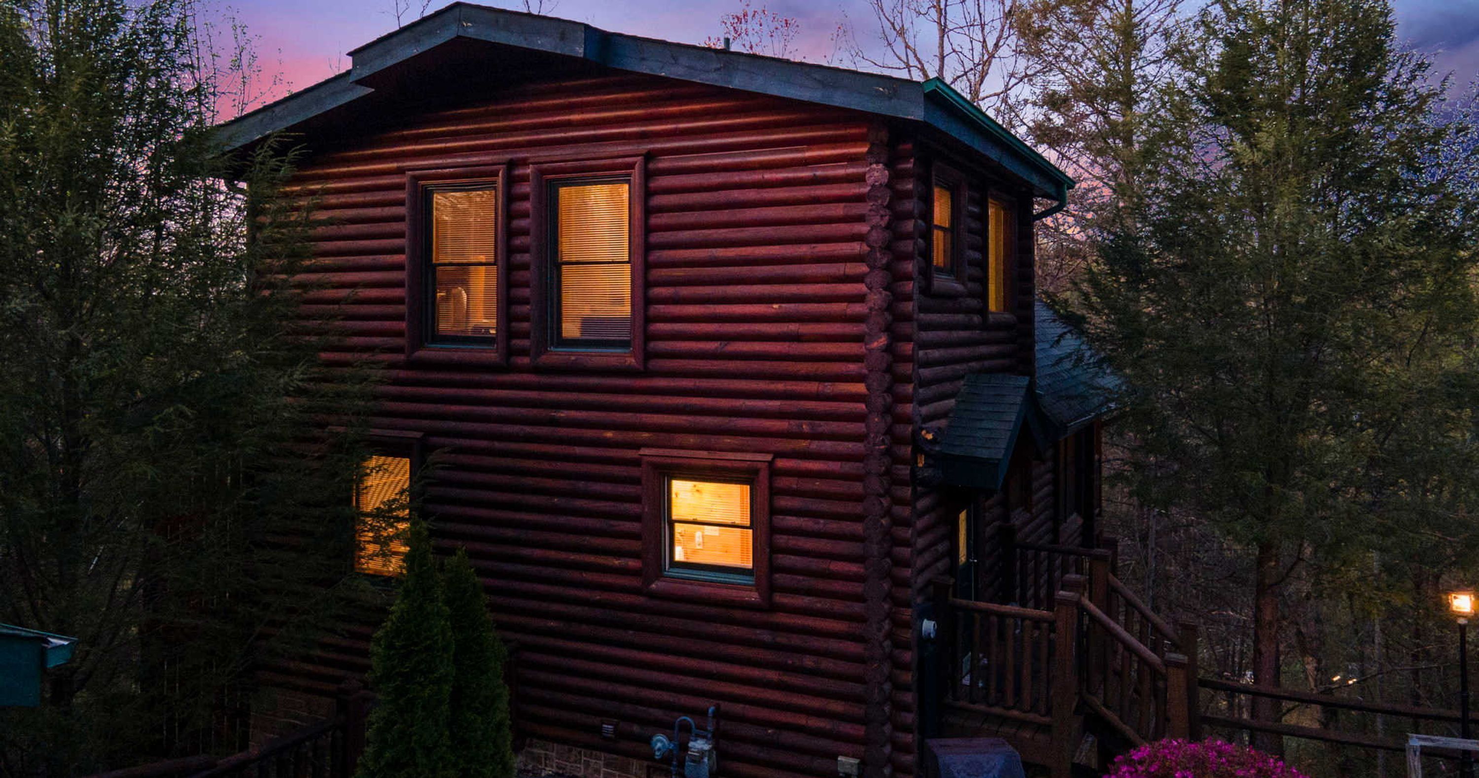 A log cabin with two windows, a porch, and a staircase leading to the upper level.