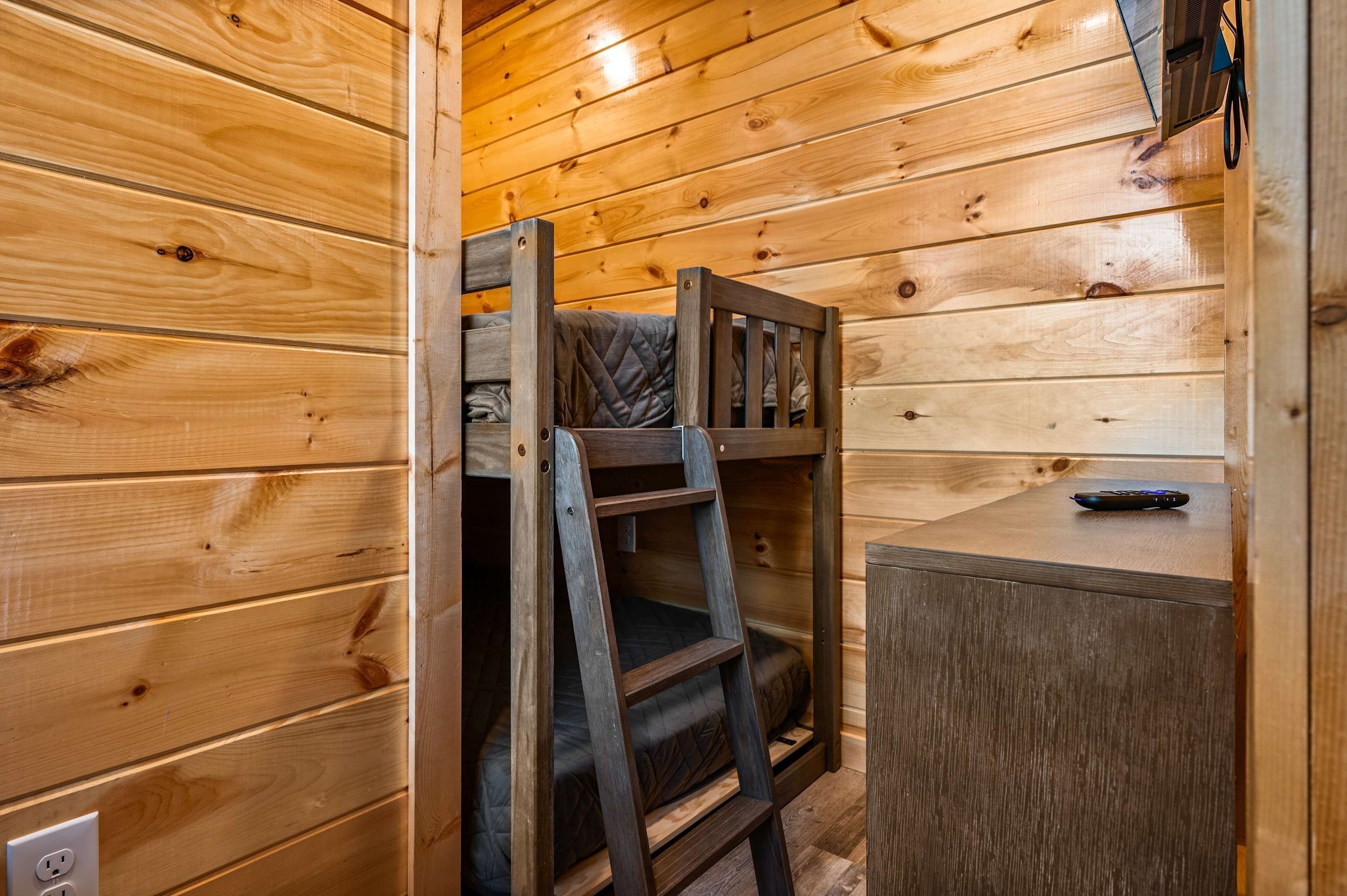 L’intérieur d’une cabane en bois, avec un lit superposé, une échelle, un petit bureau et une télécommande posée sur le bureau.