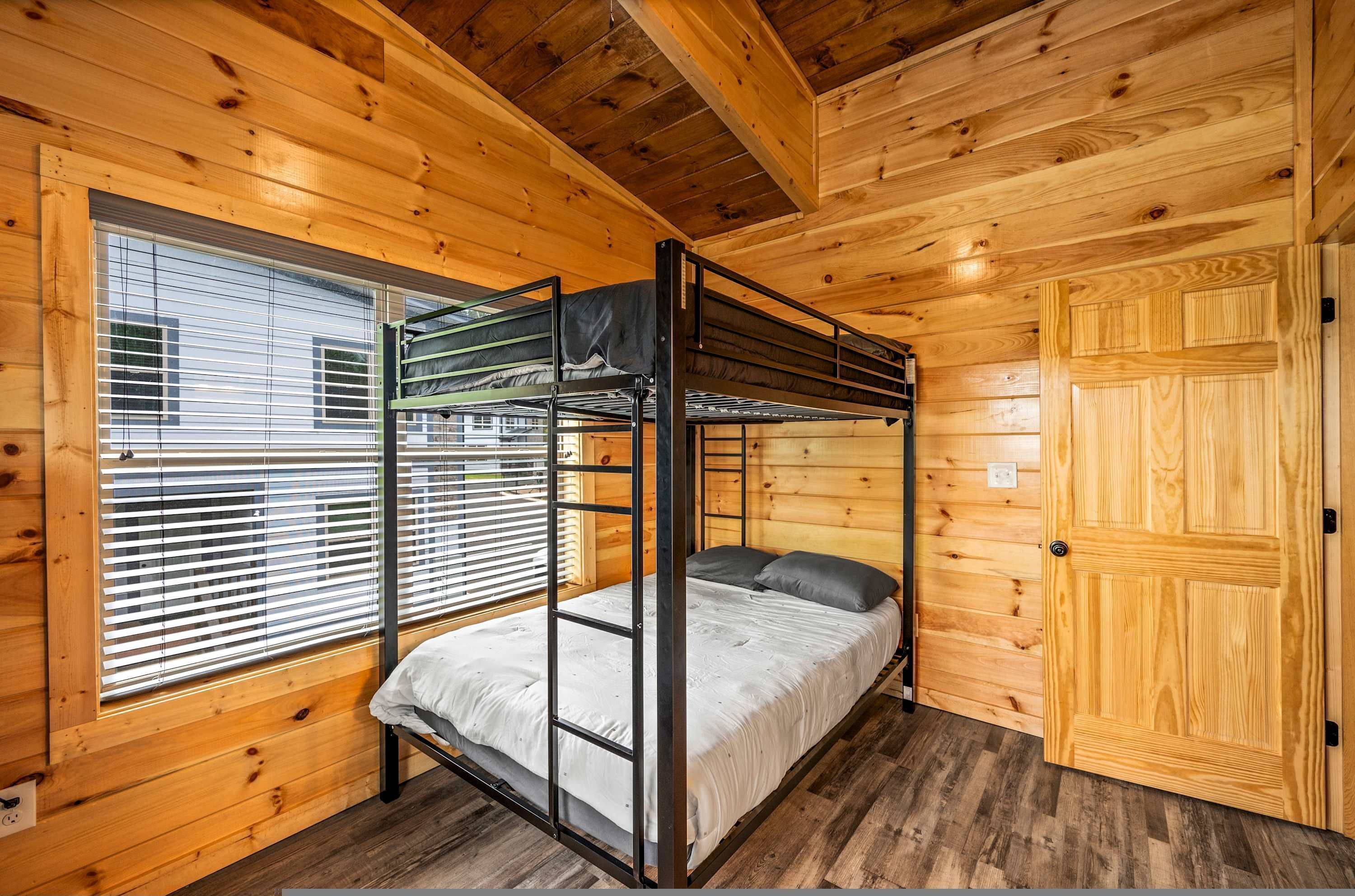 Camera con letto a castello, pareti in legno, una finestra con persiane e una porta.