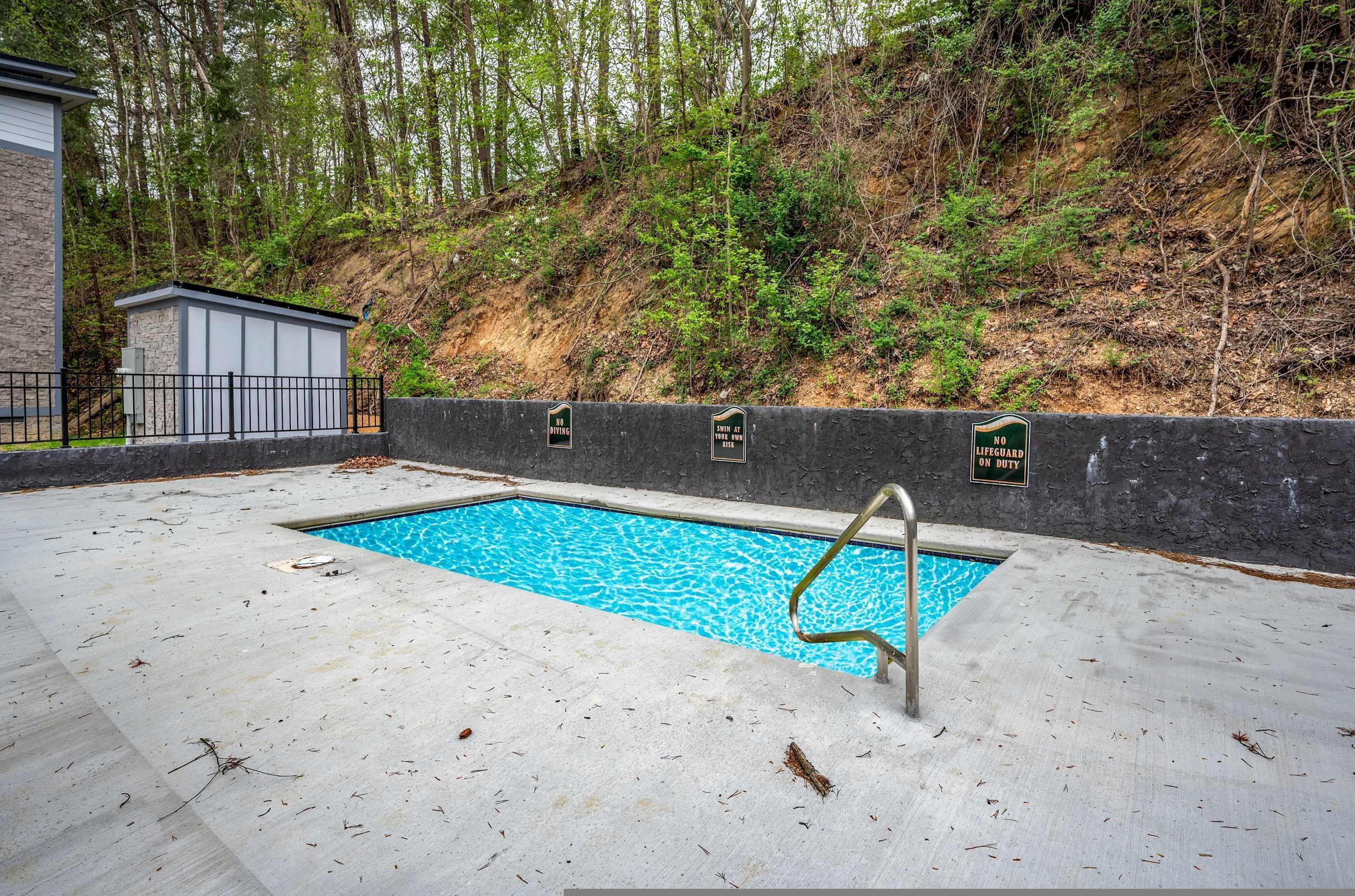 A swimming pool with a metal ladder, surrounded by a concrete deck and a stone wall.