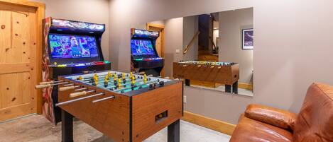A room with two foosball tables, a leather couch, and a wooden cabinet.