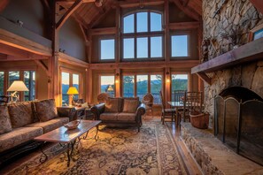 A spacious living room with a stone fireplace, large windows, and a cozy seating area. - Luxury Lakeview Cabin With Hot Tub and Game Room (Bryson City)