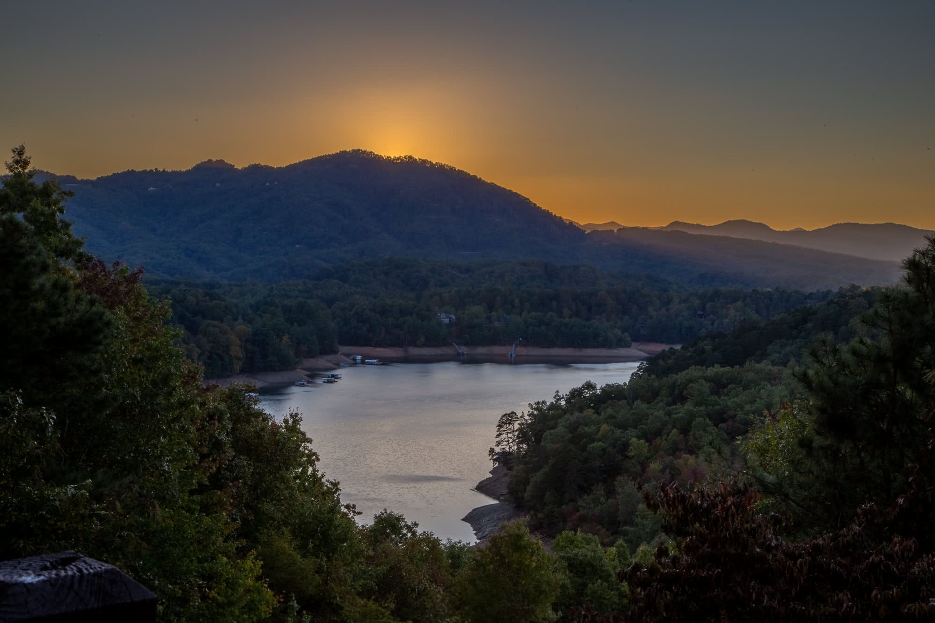 A serene lakeside view with mountains in the background and dense forest on the sides.