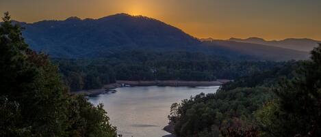 A serene lakeside view with mountains in the background and dense forest on the sides.