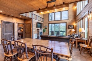 Una habitación amplia con una gran mesa de madera para comer rodeada de sillas rústicas, una chimenea y una zona de estar acogedora con un sofá y sillones.