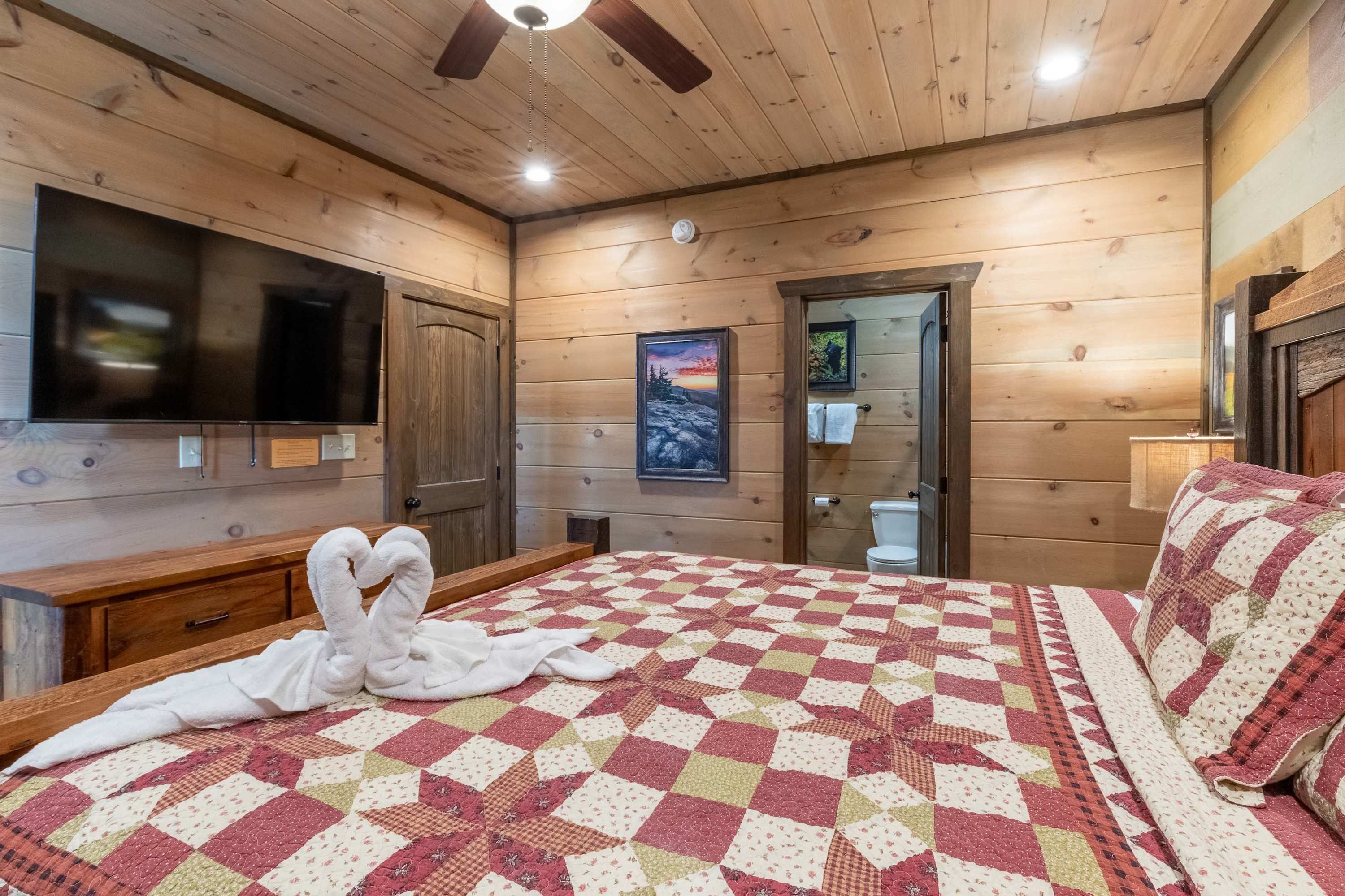 A wooden cabin bedroom with a large bed, a flat-screen TV, a painting, and a wooden door.