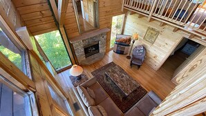 Ein Holzblockhaus-Innenraum mit Kamin aus Stein, einer Couch, einem Fernseher und einem Essbereich.