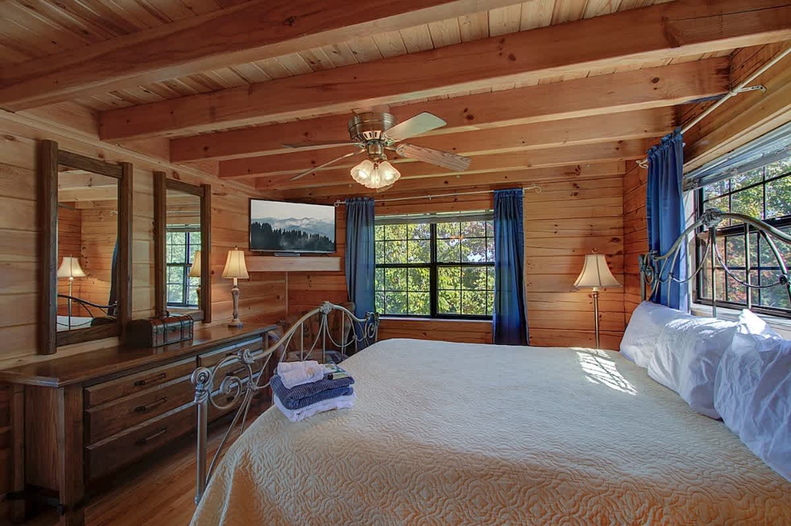 A wooden cabin bedroom with a bed, dresser, mirror, and a ceiling fan.