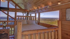 Ein Schlafzimmer einer Holzhütte mit großem Fenster und Blick auf die Landschaft.