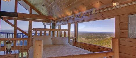 A wooden cabin bedroom with a large window offering a view of the landscape.