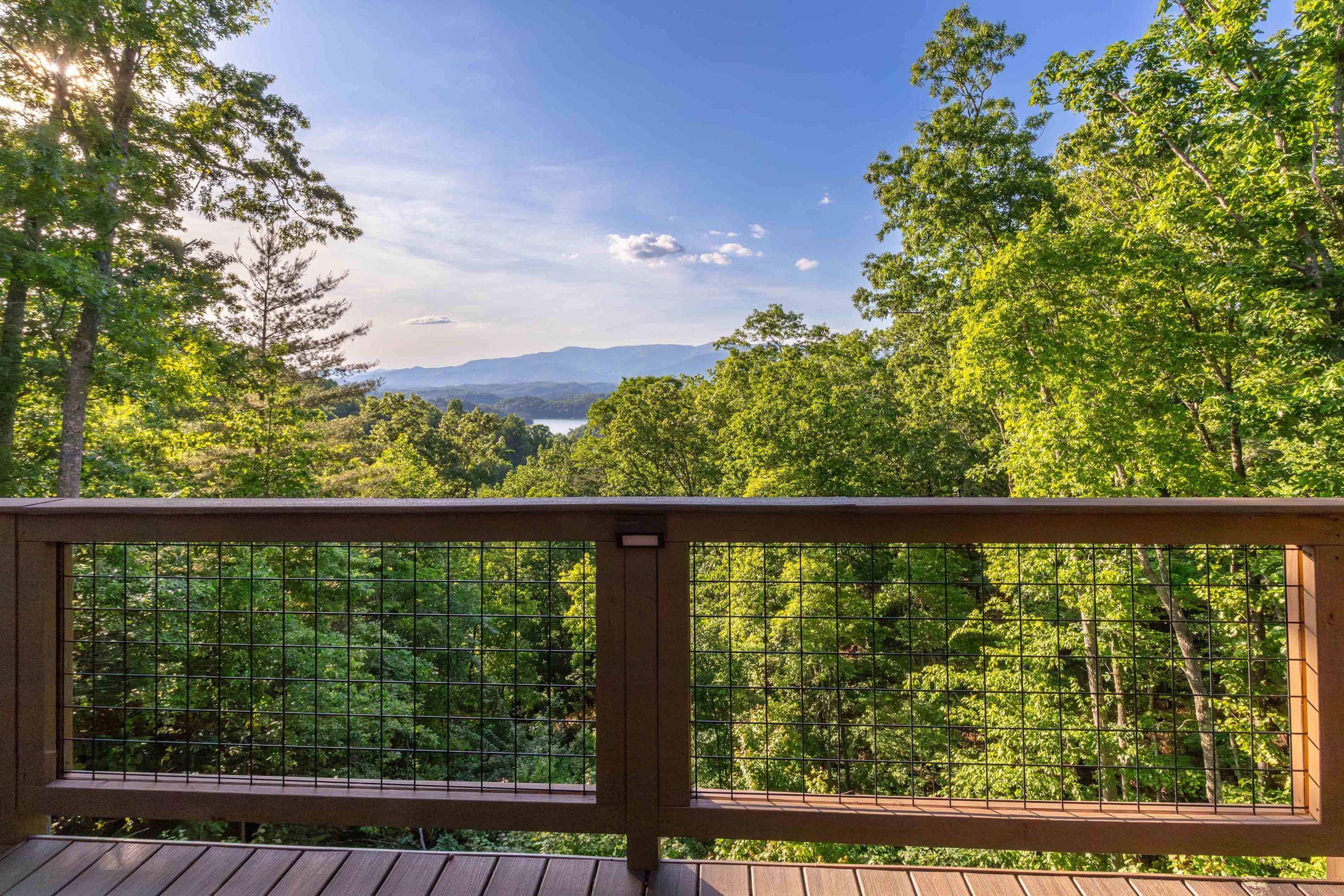 A wooden deck with a metal railing overlooking a dense forest and a distant mountain range.