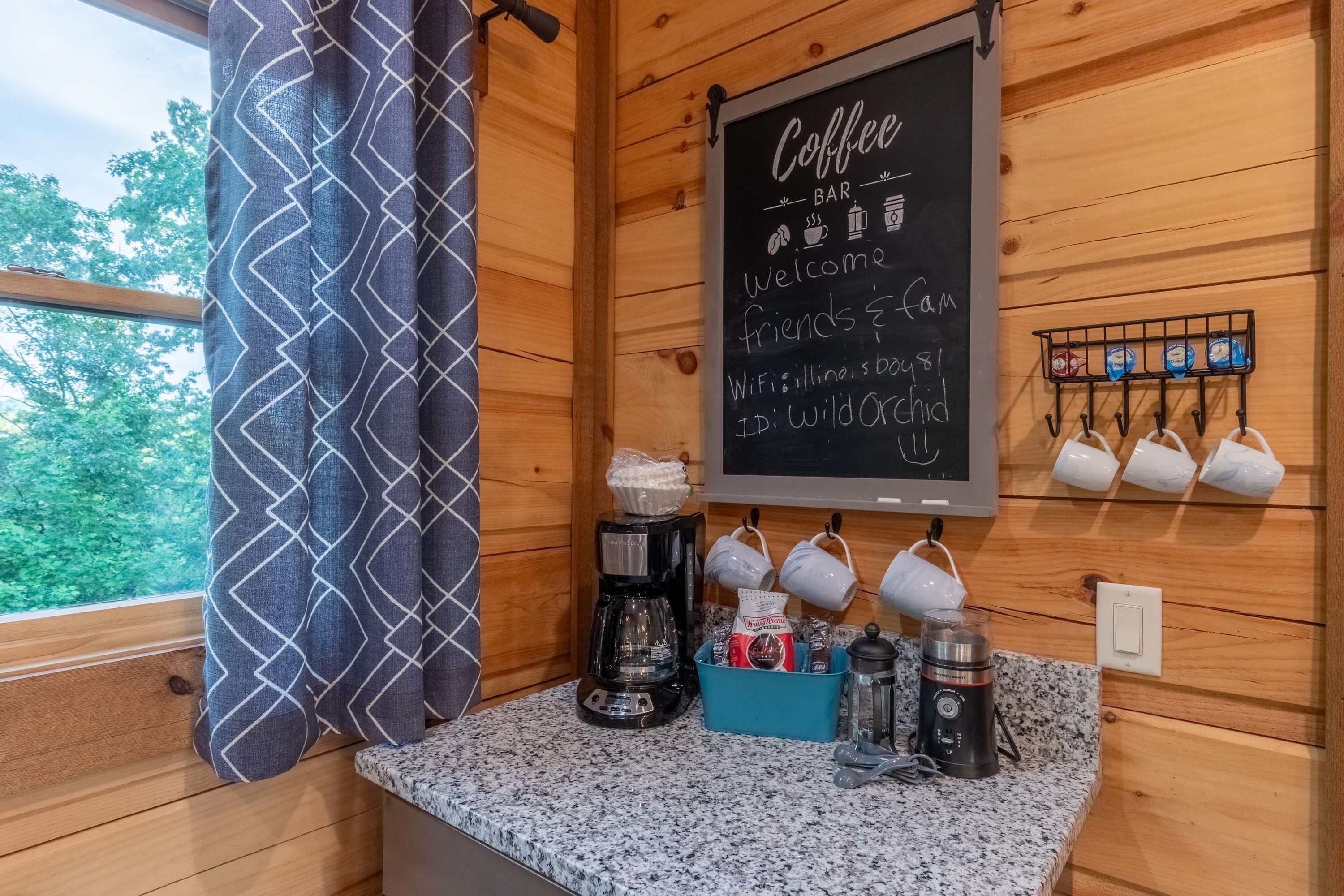 Een knus interieur met een koffiebar, een krijtbordmenu en een raam met uitzicht op bomen.