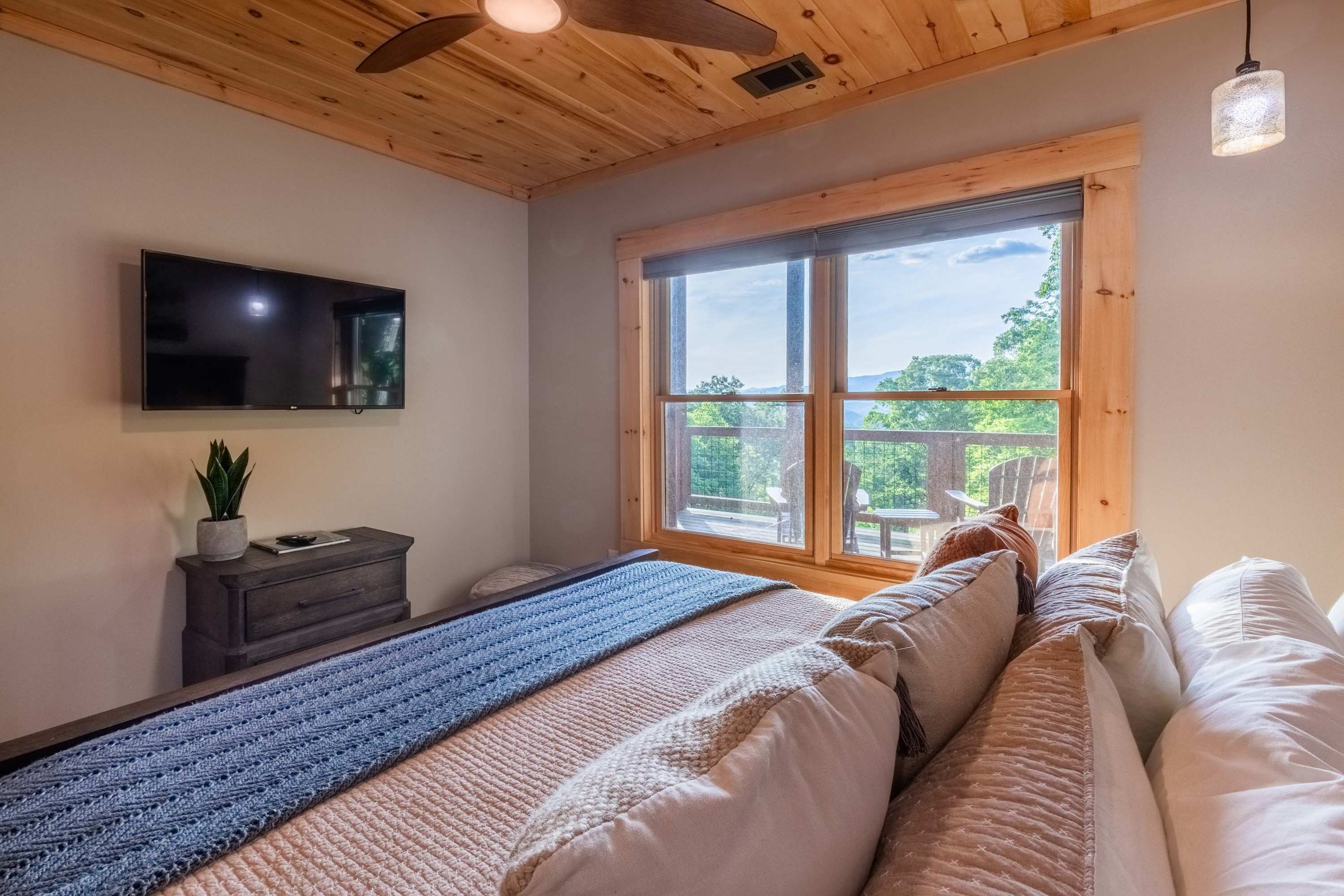 Een slaapkamer met een groot raam, een flatscreen televisie, een donker houten dressoir en een blauw gebreid vloerkleed.