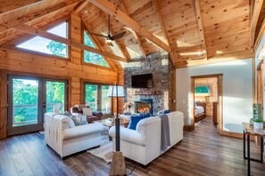 Un salón espacioso con chimenea de piedra, vigas de madera y ventanas grandes.
