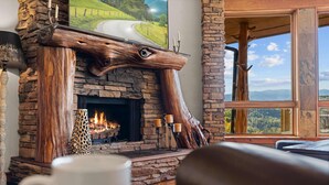 Ein Kamin aus Stein mit Holzverkleidung, eine weiße Tasse im Vordergrund und eine herrliche Aussicht durch ein großes Fenster.