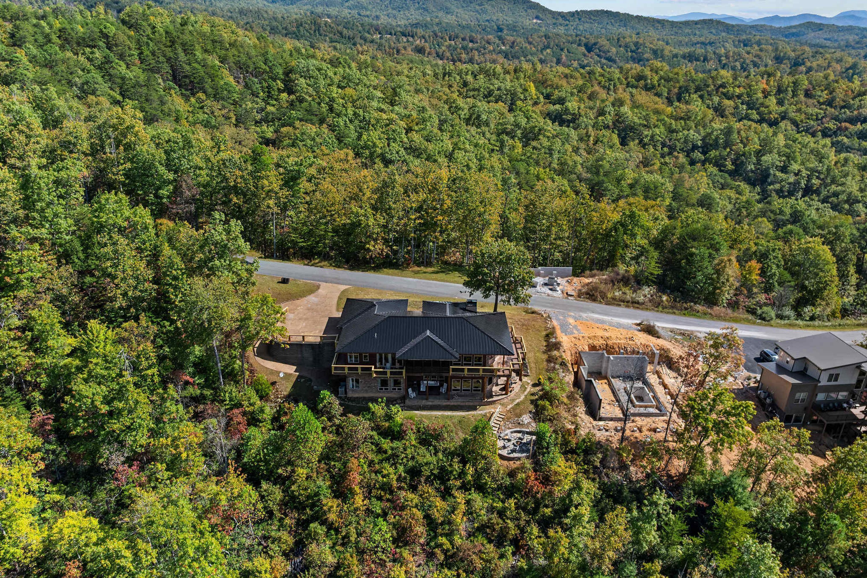 A large, modern lodge with a prominent black roof, surrounded by dense forest and mountains.