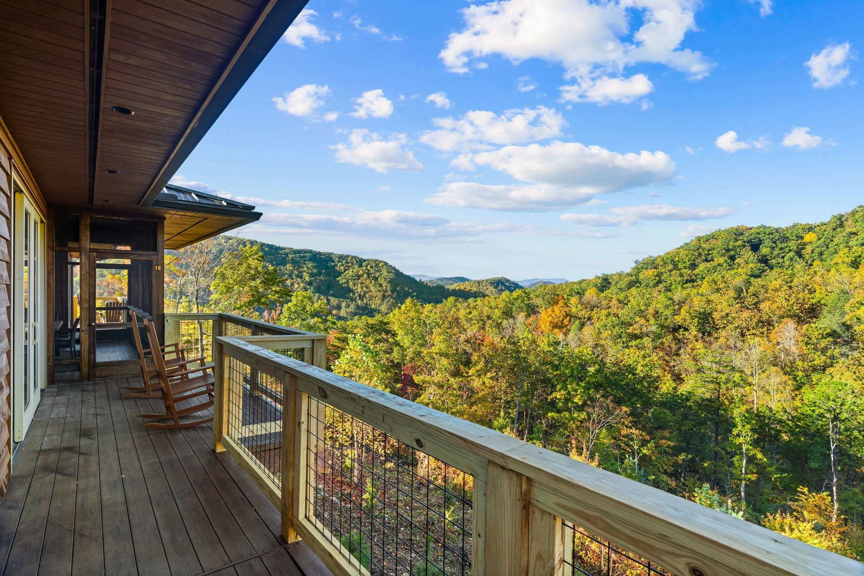 A wooden deck with a railing overlooking a forested mountain range.