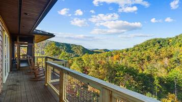 A wooden deck with a railing overlooking a forested mountain range.