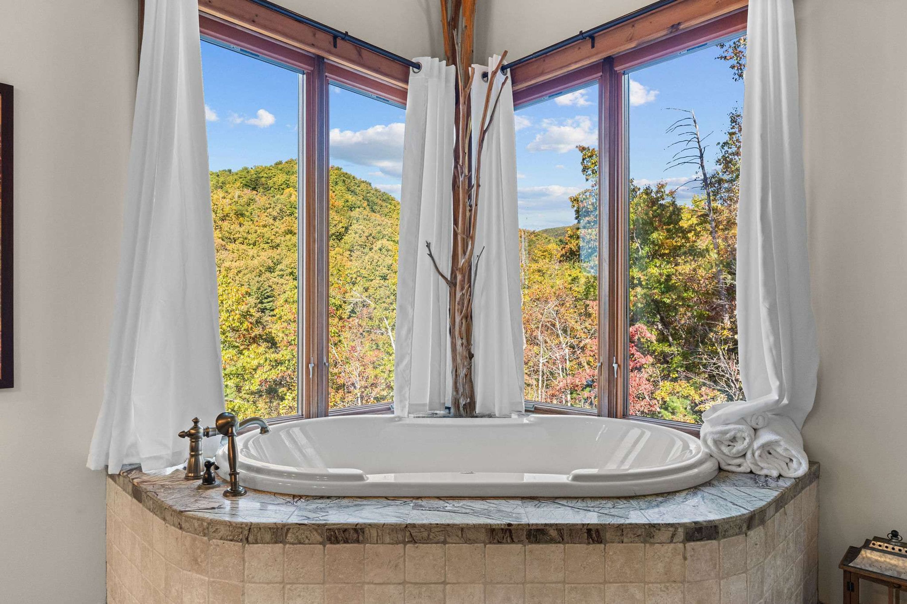 A bathroom with a freestanding bathtub, large windows, and a view of a forested hillside.