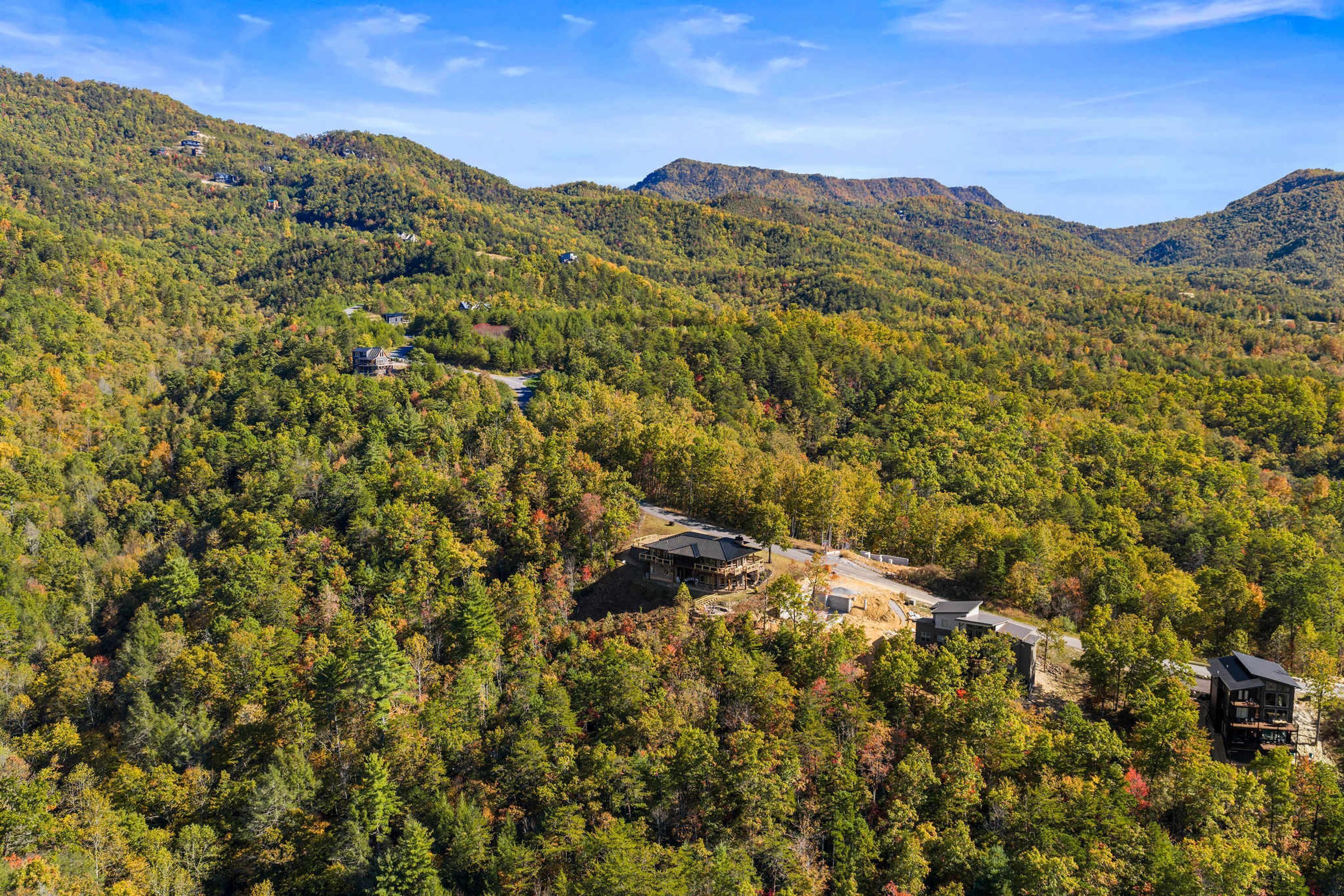 A lodge nestled in a forested valley with multiple buildings, surrounded by dense trees and hills.