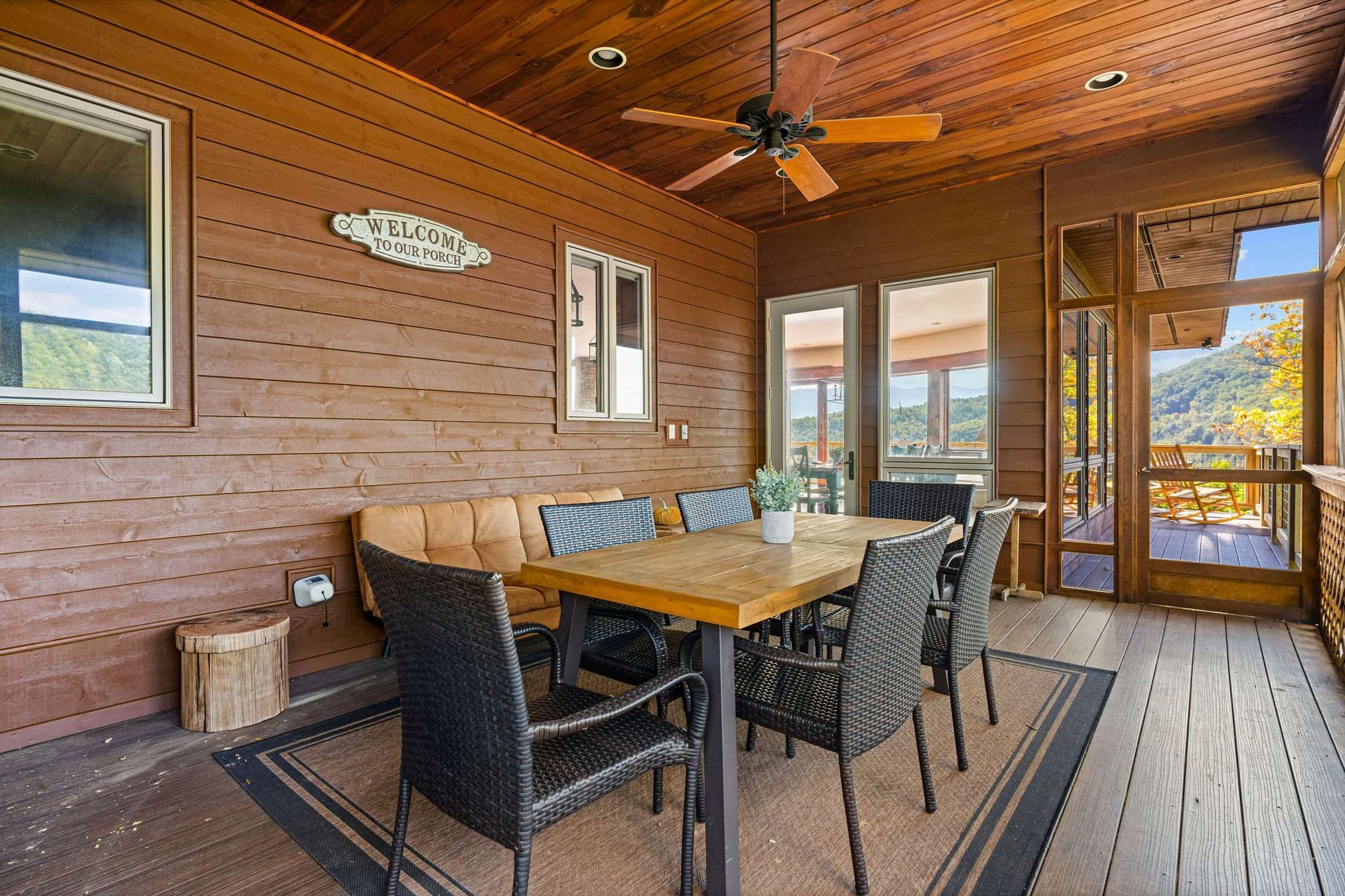 Een houten interieur met een houten tafel en stoelen, een plafondventilator en een bord met de tekst 'WELCOME TO OUR PORCH'.