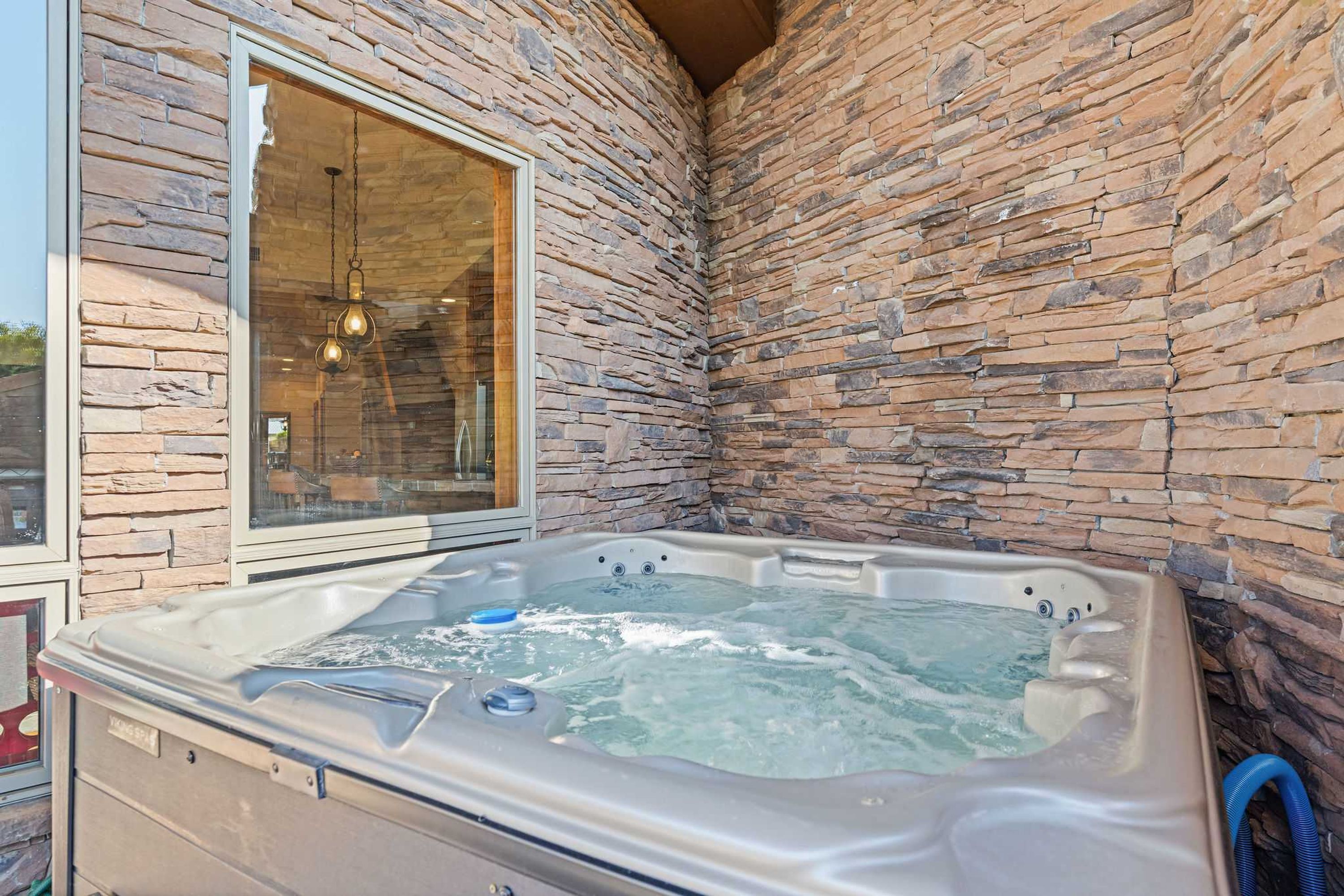 Un jacuzzi en un espacio al aire libre con paredes de piedra y un ventanal grande.