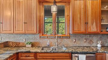 A kitchen with wooden cabinets, a granite countertop, a stainless steel sink, and a window with a view of greenery.