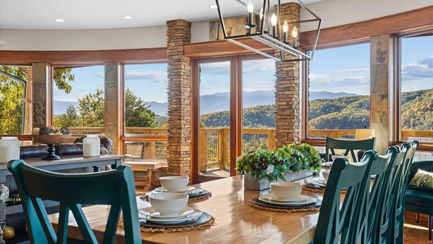 Ein Essbereich mit Holztisch, gedeckt für vier Personen, große Fenster mit Blick auf die Berge und Steinpfeilern.