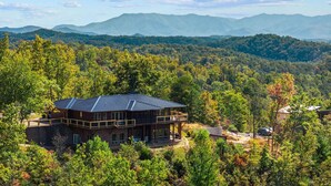 Eine zweistöckige Lodge mit Metalldach, umgeben von dichtem Wald und Bergen im Hintergrund.