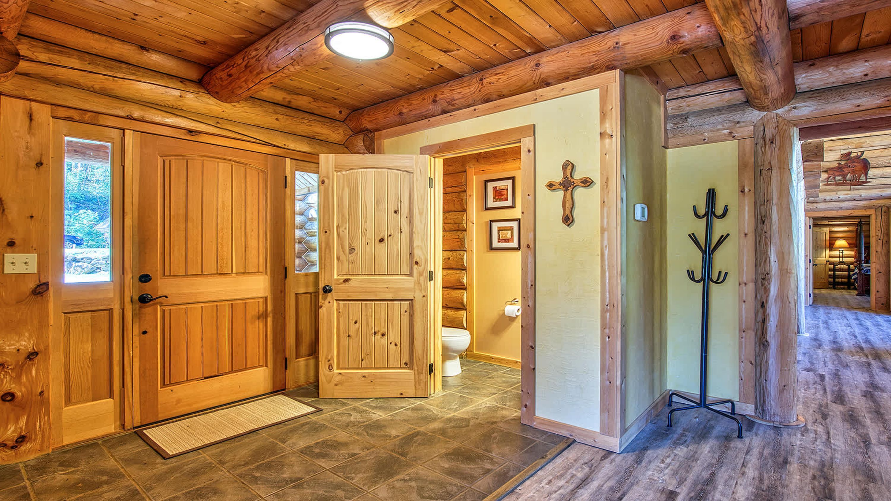 A wooden interior with a large door, a small bathroom, and a coat rack.