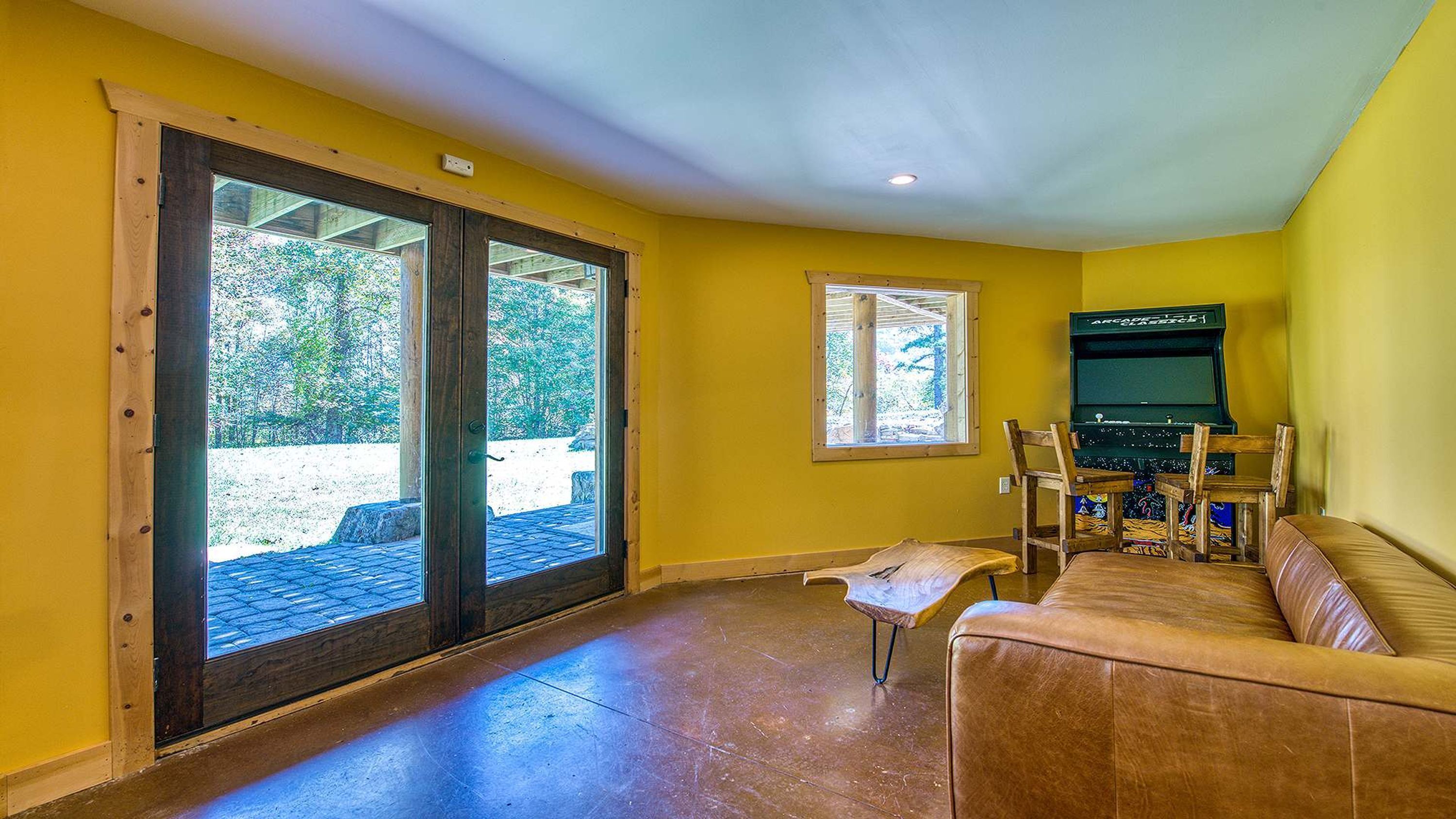 A room with a sliding glass door leading to an outdoor area, a small table with chairs, and a gaming console.