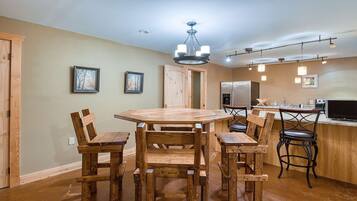 A dining area with a wooden table and chairs, a kitchen with appliances, and framed pictures on the wall.