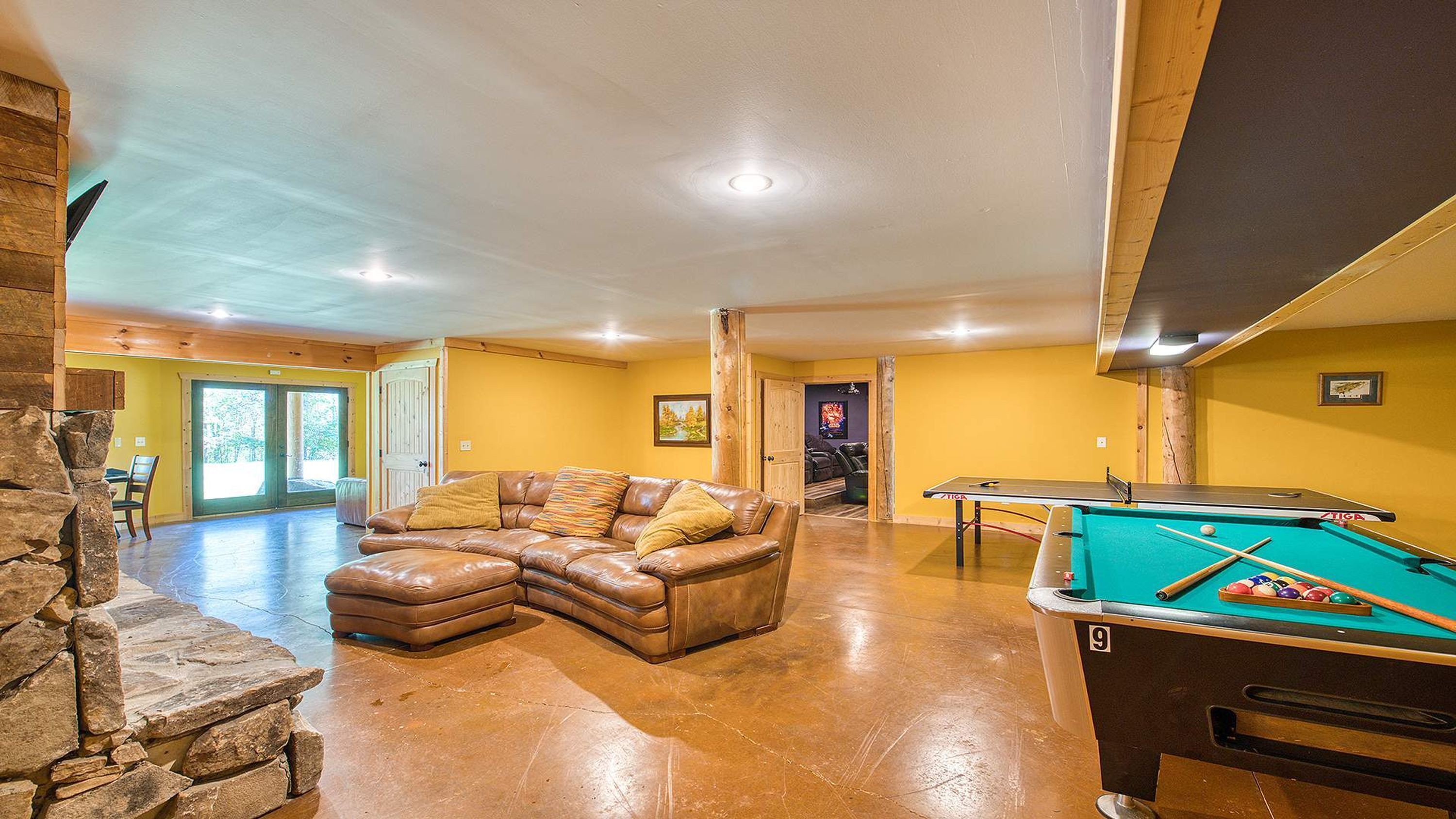 A spacious living room with a leather sectional sofa, a pool table, and a stone wall.