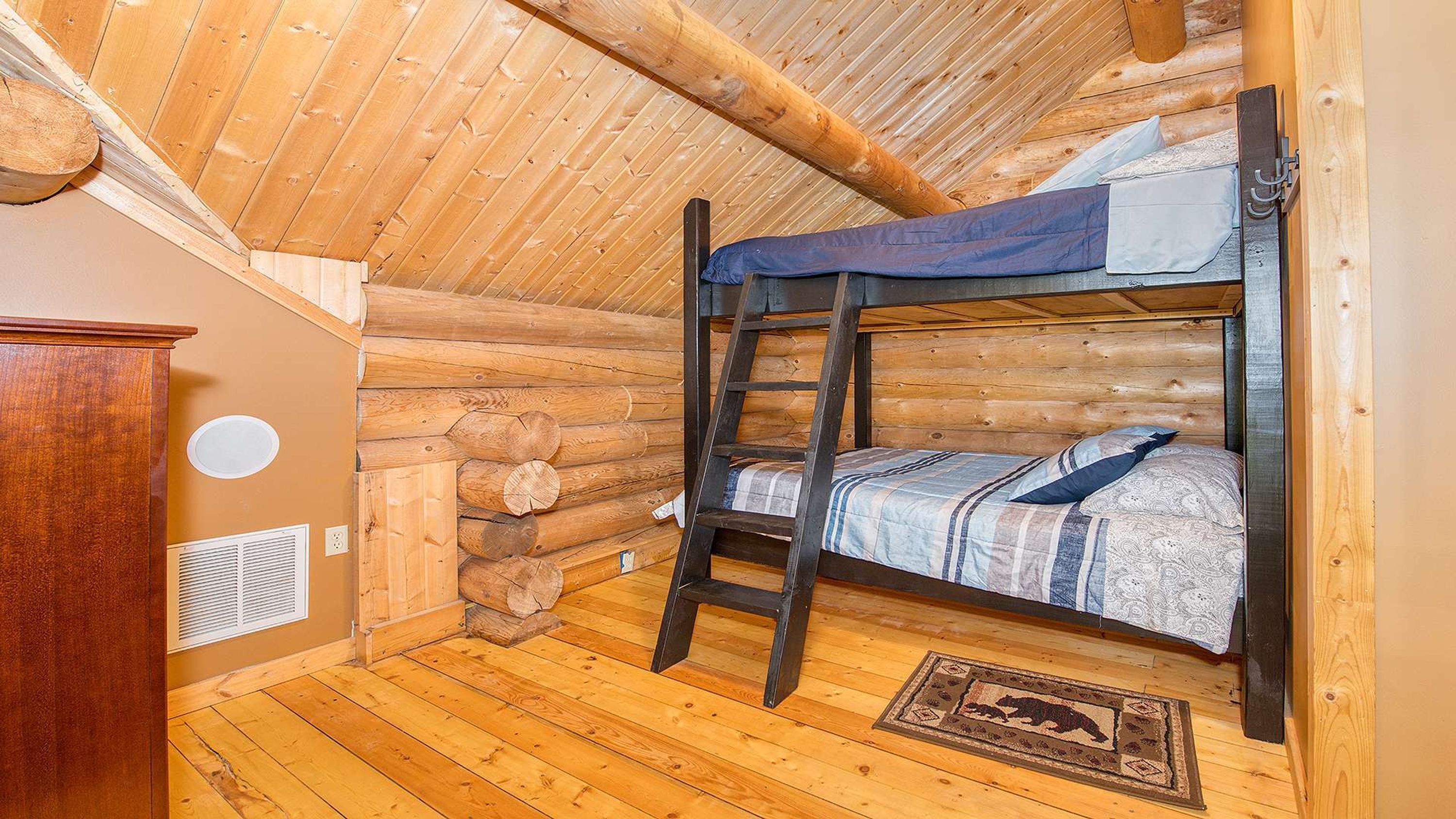 Une chambre dans un chalet en rondins, avec un lit superposé, des murs en bois et un plancher en bois.
