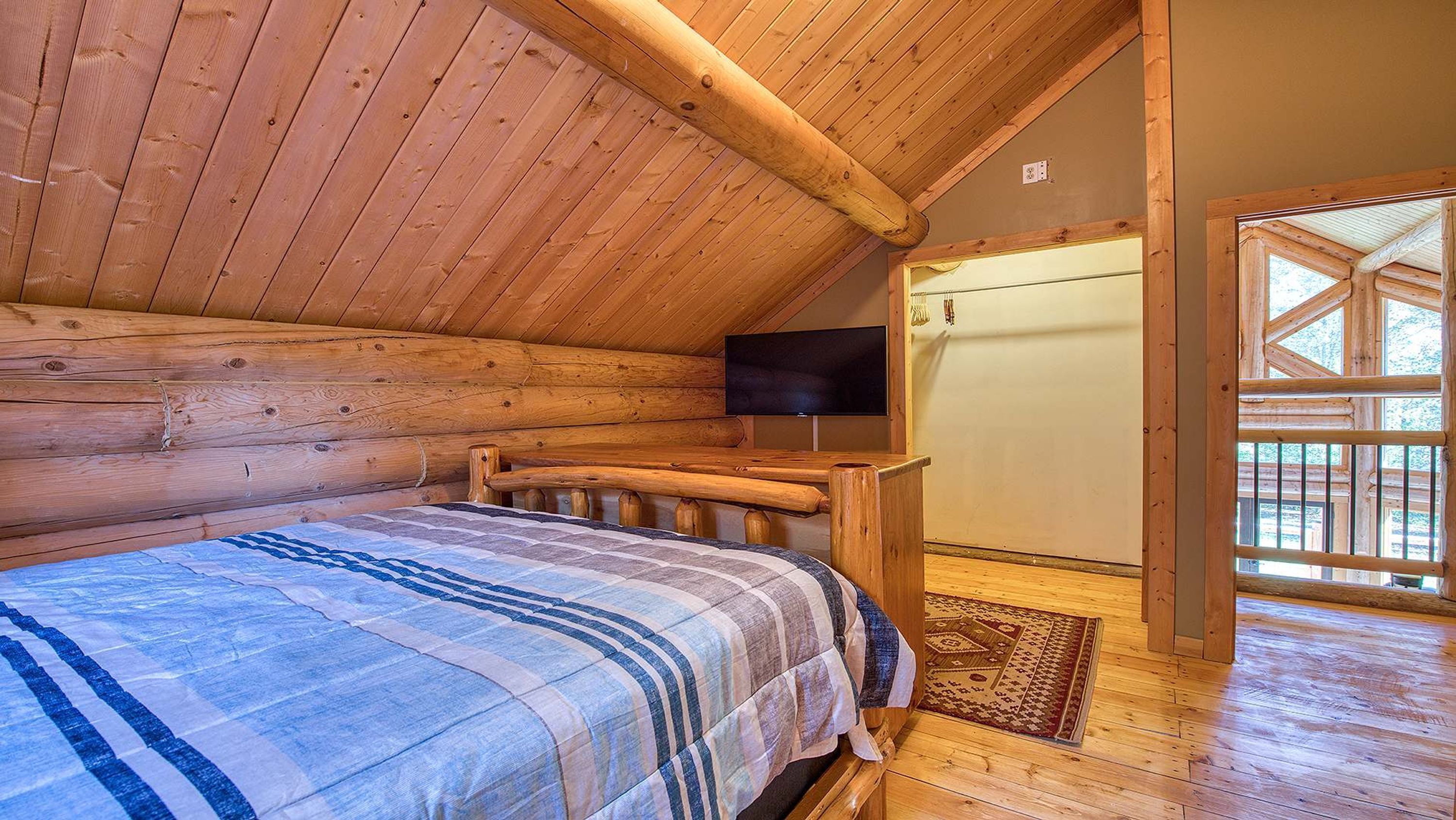 A log cabin bedroom with a bed, wooden walls, a television, and a door leading outside.