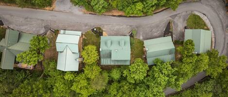 An aerial view of a residential area with multiple houses, each with a green roof, surrounded by dense green trees.