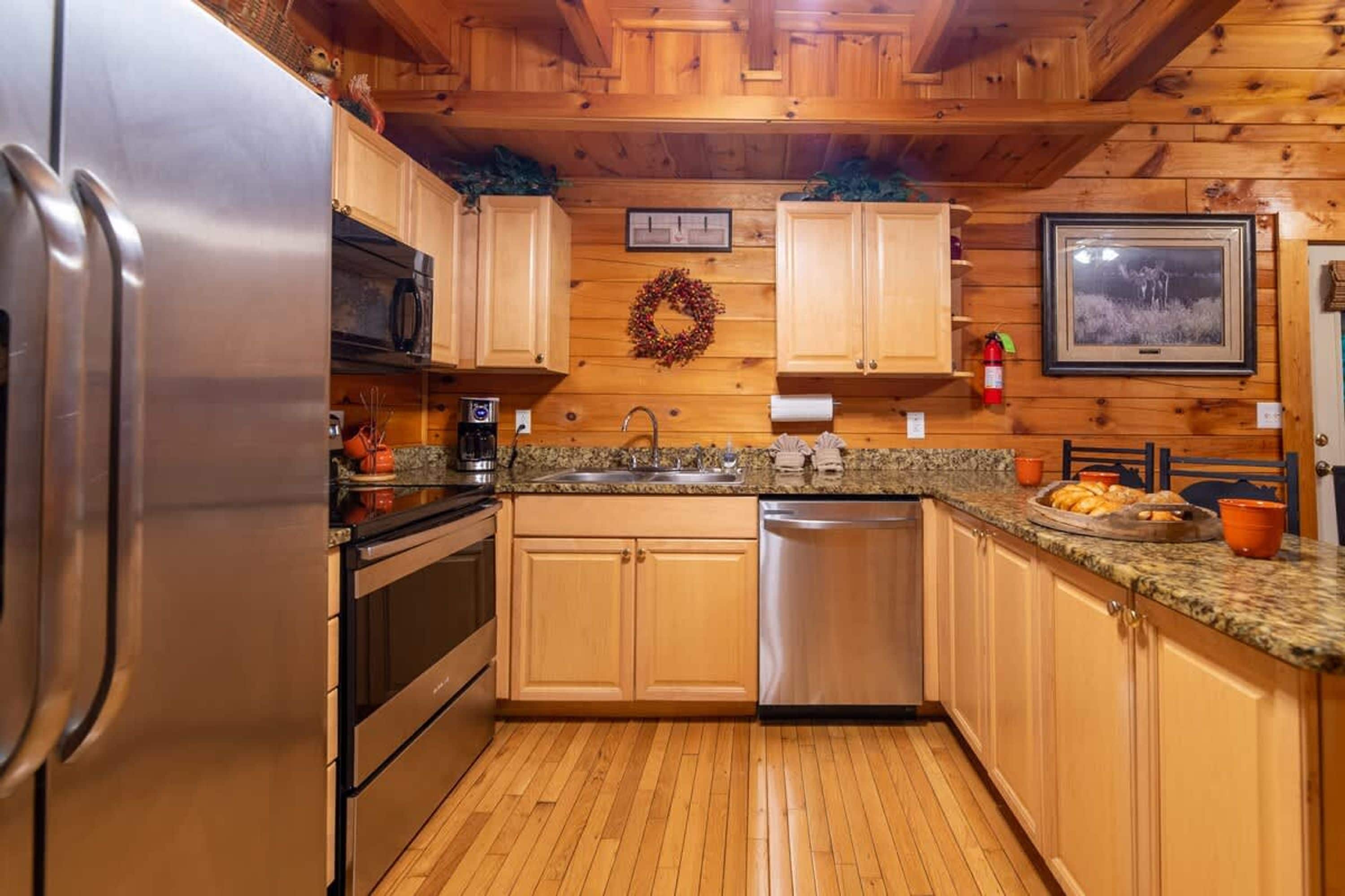 A kitchen with wooden cabinets, stainless steel appliances, granite countertops, and a wooden floor.