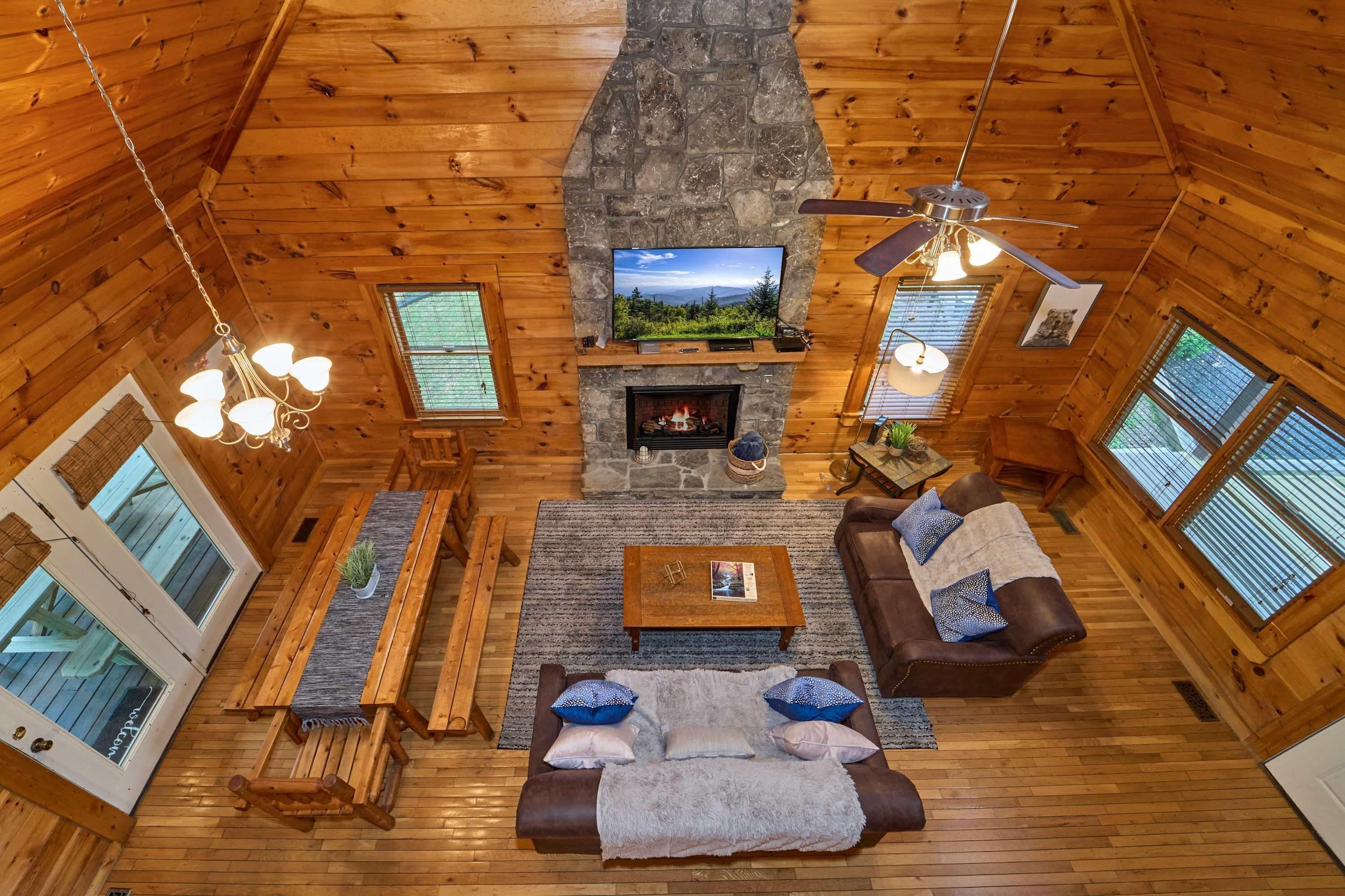 A cozy cabin interior with a stone fireplace, wooden walls, a television, and a seating area with a sofa and coffee table.