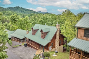 Un chalet doté d’un toit en métal vert, de cabanes en bois et offrant une vue sur une chaîne de montagnes boisées.
