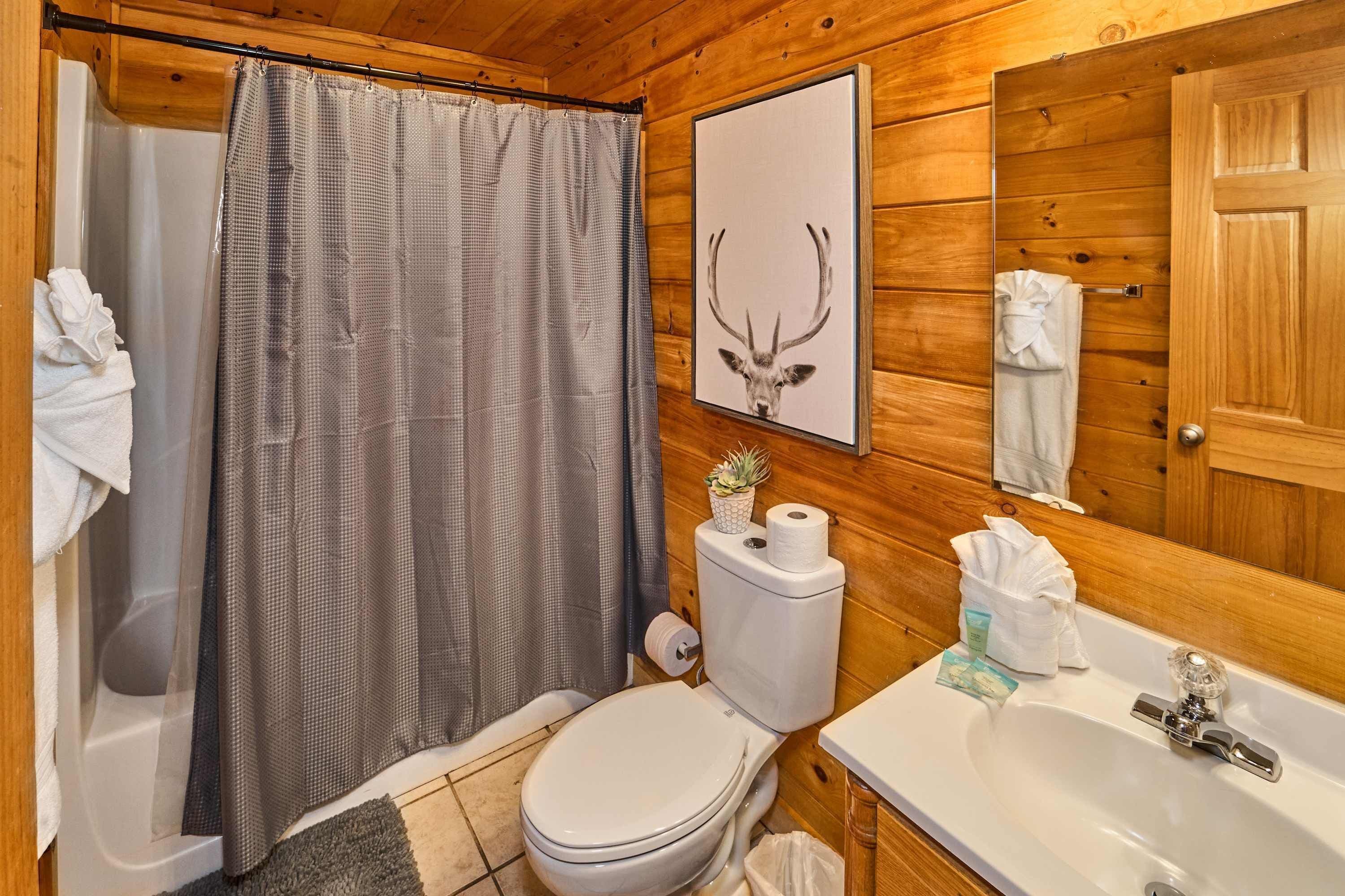 A wooden cabin bathroom with a shower curtain, toilet, sink, and a framed deer antler picture.