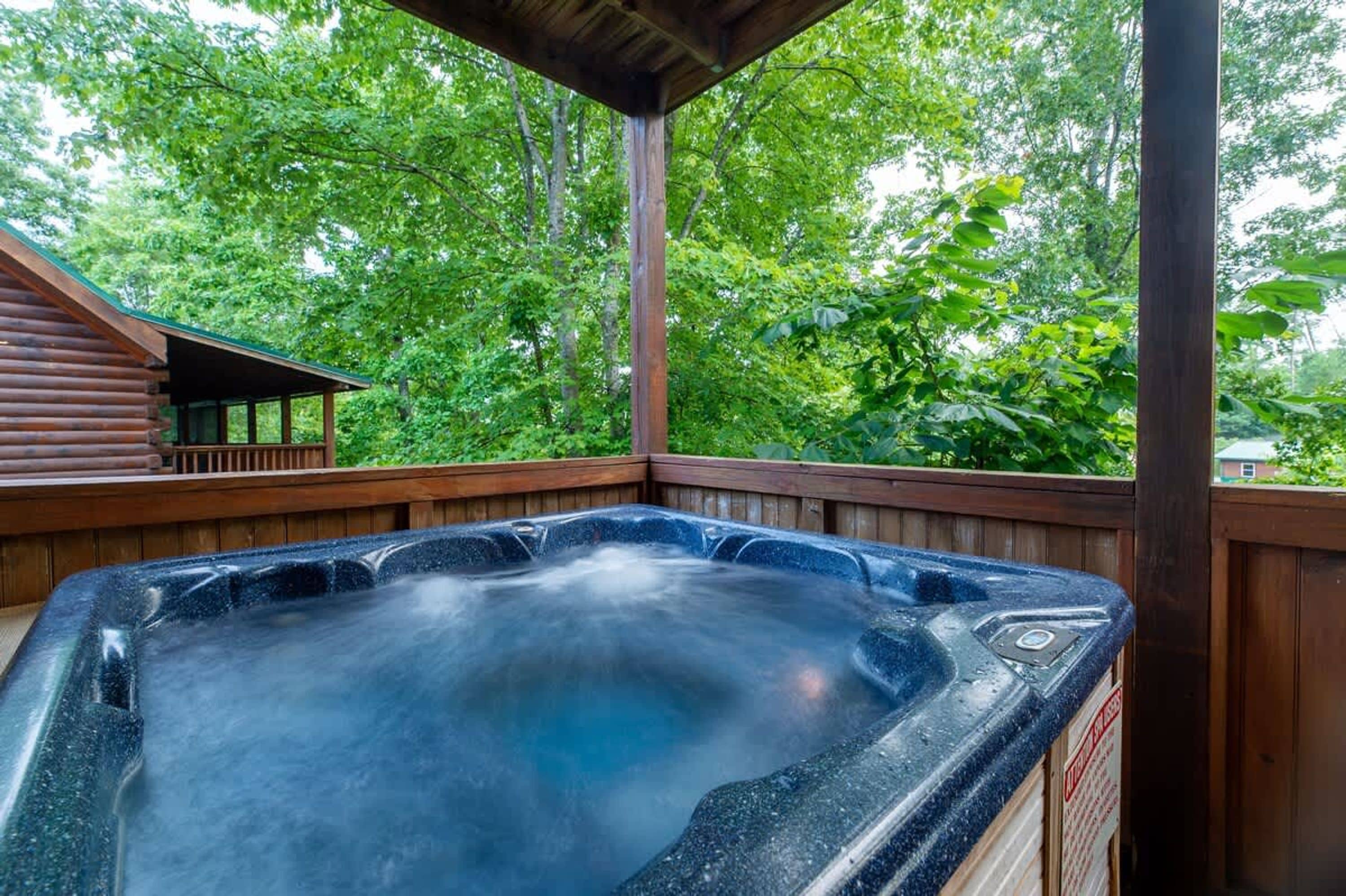 A hot tub with a wooden deck and a view of lush green trees.