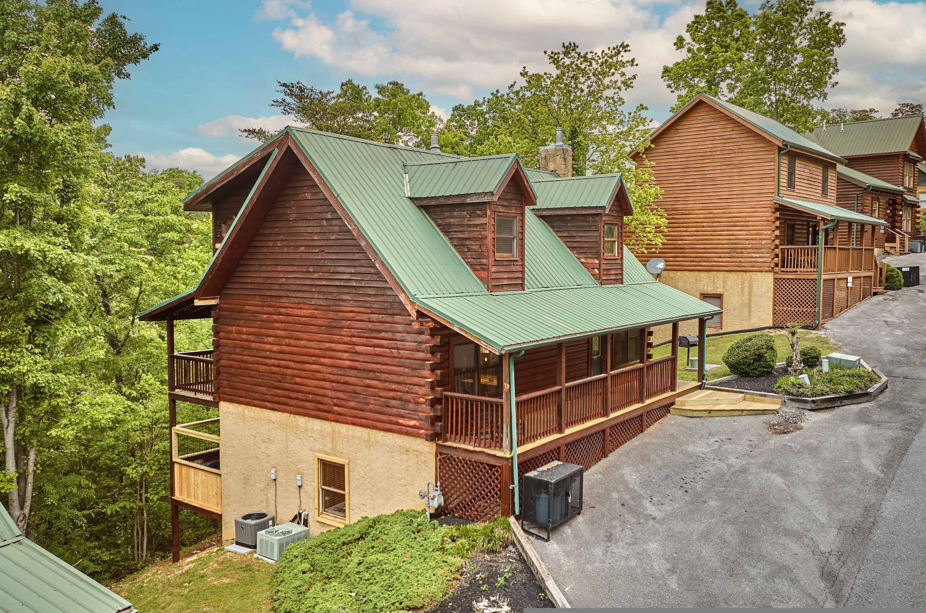 A log cabin-style building with a green metal roof, a balcony, and a small garden area.